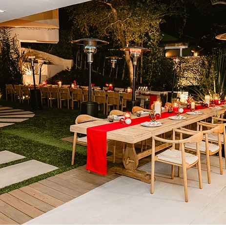Outdoor dining area with long wooden tables decorated with red table runners.