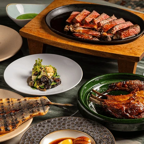 Assorted gourmet dishes including grilled steak, roasted meat, vegetables, and fish served on elegant plates at a fine dining setup.