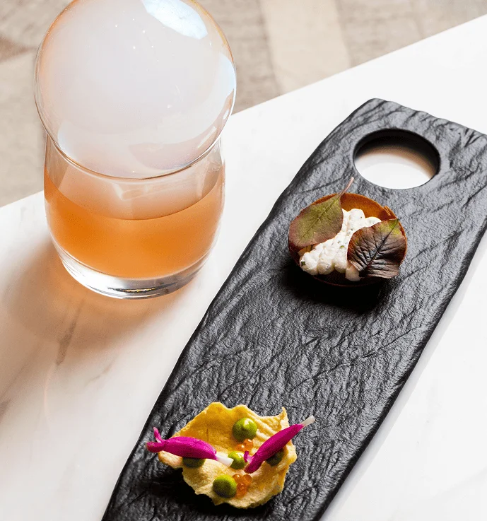 Gourmet appetizer platter with creative bite-sized dishes and a cocktail topped with smoke.