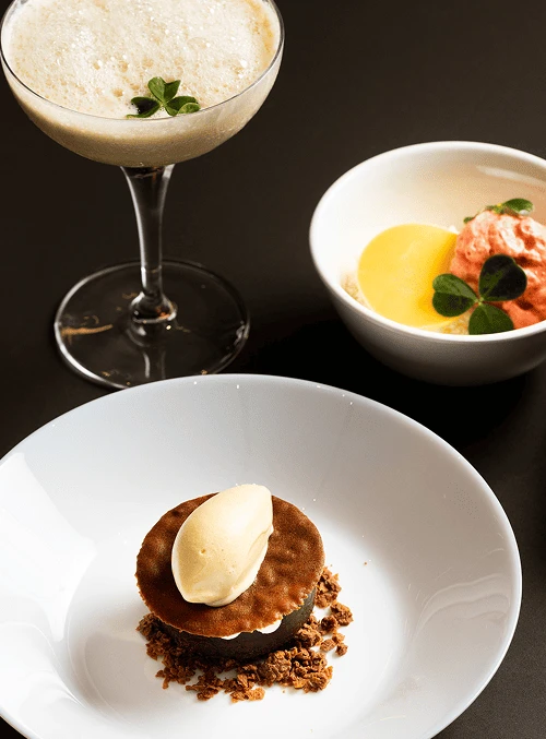 Gourmet dessert trio with a plated tart topped with ice cream, a creamy bowl dessert with garnish, and a frothy cocktail in a glass.